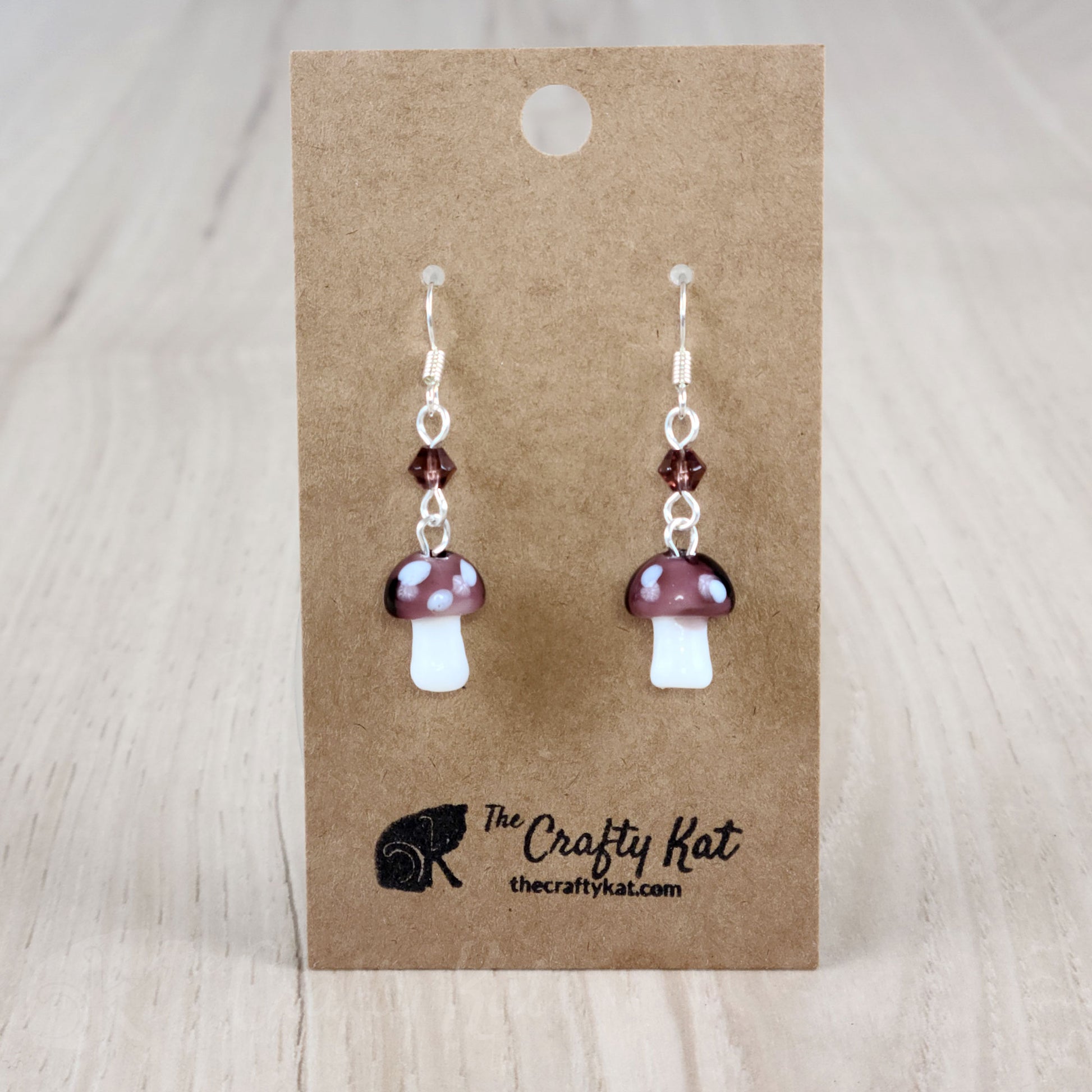 Mushroom-shaped tiered earrings made of lampwork and pressed glass beads with silver-plated base metal fittings. These mushrooms are amethyst (purple) with white spots.