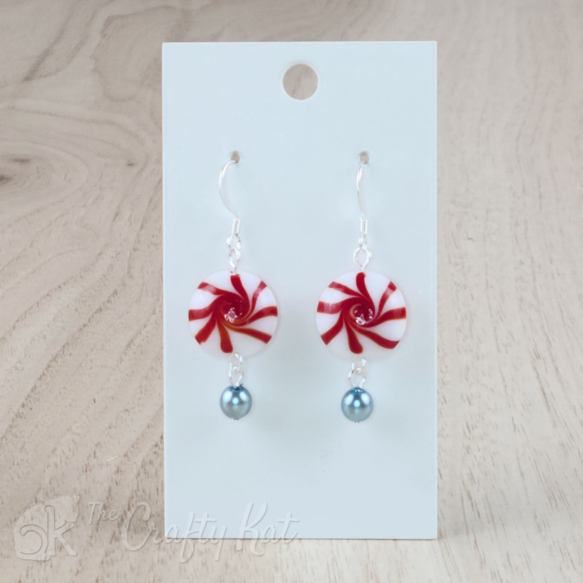 A pair of earrings featuring lampwork glass beads in the shape of classic "starlight" peppermint candies, accented with a light blue glass pearl on silver base metal.