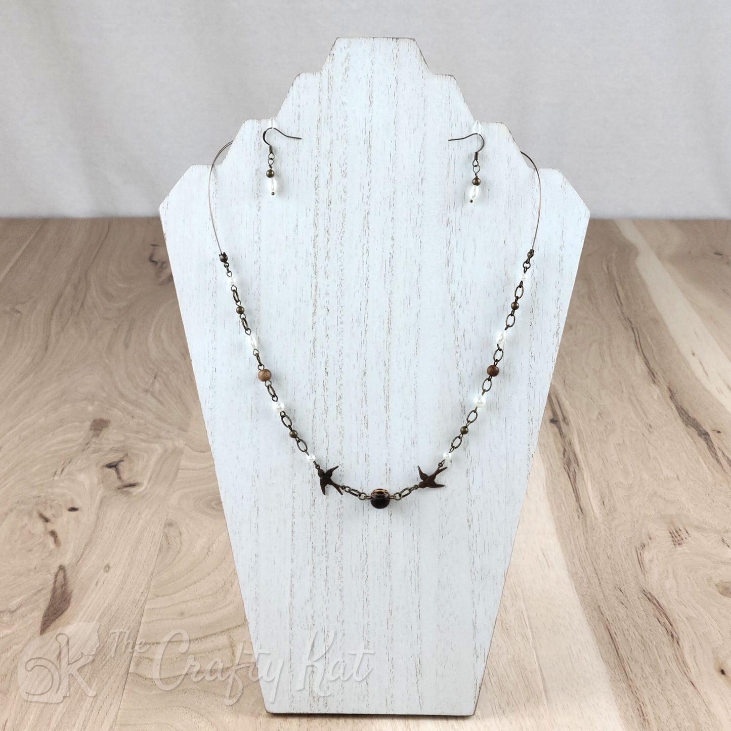 Necklace and earring set; focal of necklace is two bronze swallows with a coco wood bead between them; rest of necklace and earrings include bronze tiger tail, bronze fittings and beads, wood beads, and glass pearls