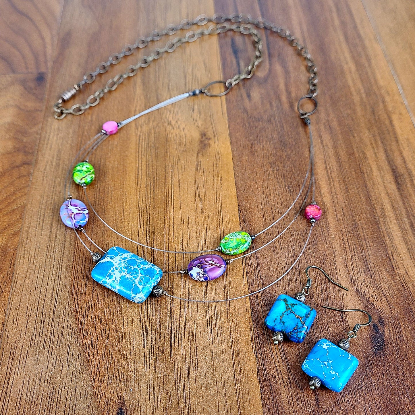 Three-layered tigertail necklace features geometric beads dyed blue, pink, green, and purple; antique copper fittings