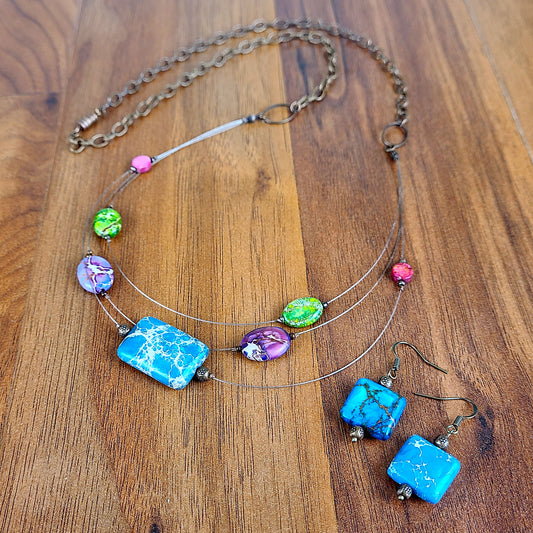 Three-layered tigertail necklace features geometric beads dyed blue, pink, green, and purple; antique copper fittings