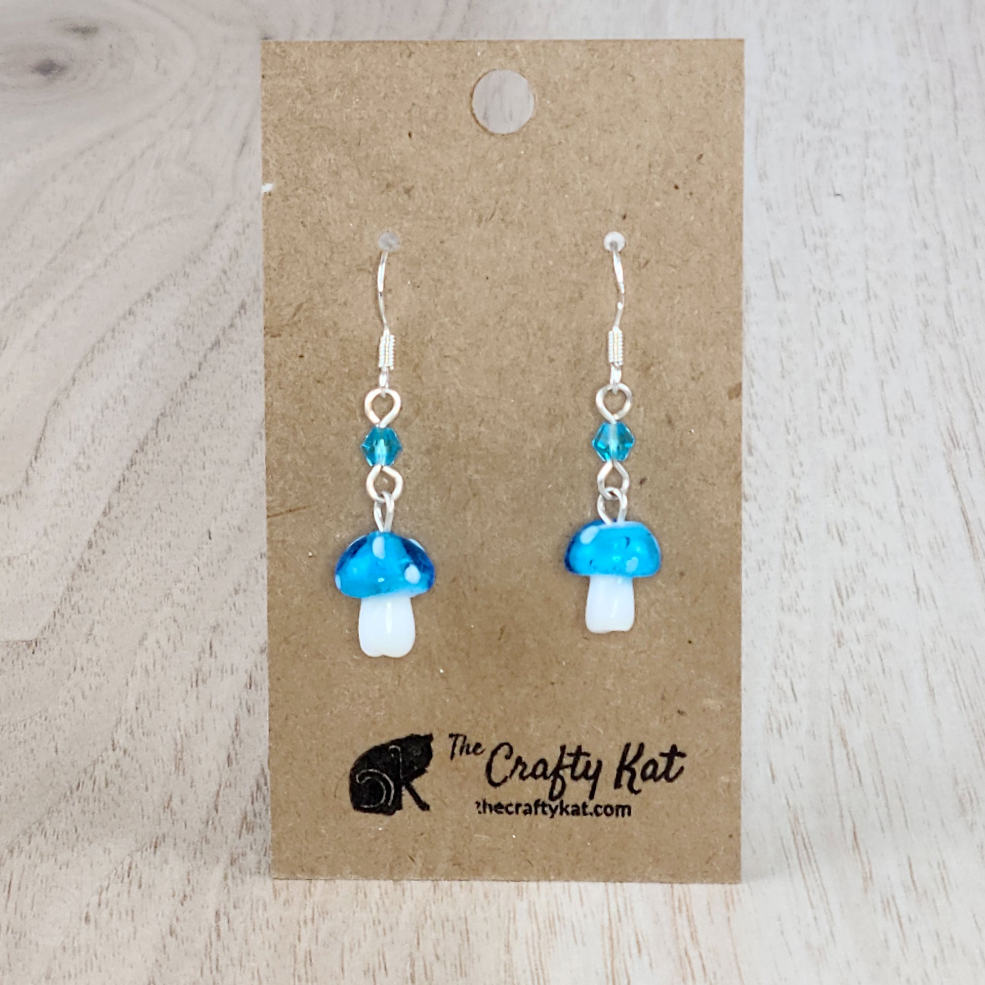 Mushroom-shaped tiered earrings made of lampwork and pressed glass beads with silver-plated base metal fittings. These mushrooms are aqua (sky blue) with white spots.