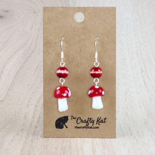 Mushroom-shaped tiered earrings made of lampwork and pressed glass beads with silver-plated base metal fittings. These mushrooms are red with white spots.