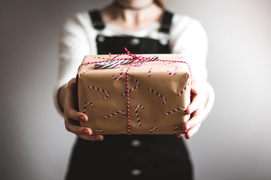 A woman holding out a festively-wrapped parcel. Photo by Kira auf der Heide on Unsplash