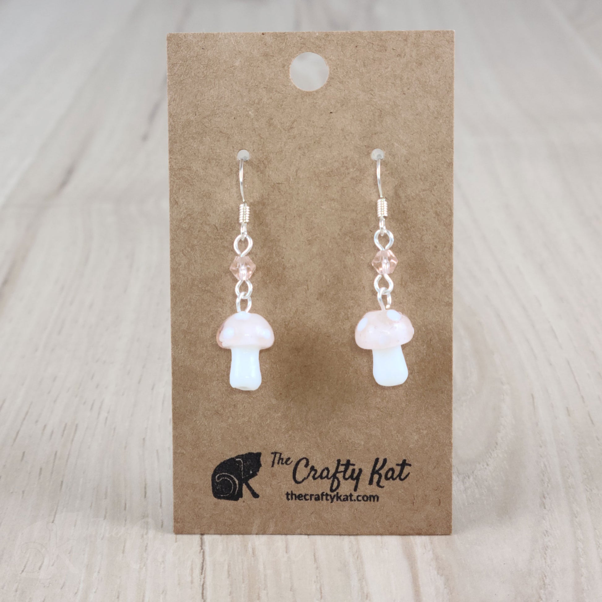 Mushroom-shaped tiered earrings made of lampwork and pressed glass beads with silver-plated base metal fittings. These mushrooms are blush pink with white spots.