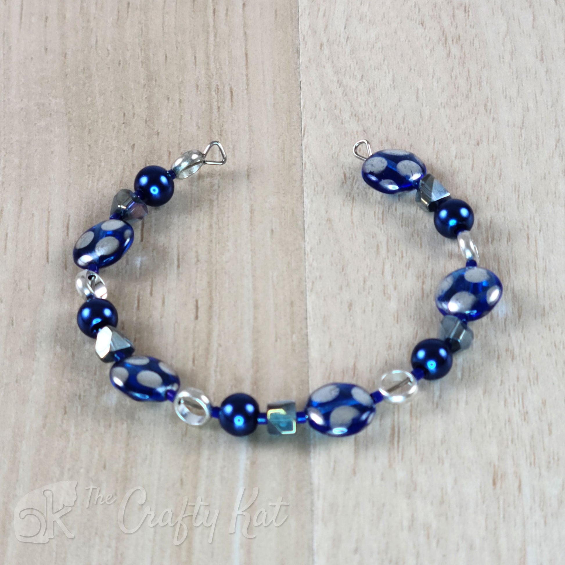 Steel memory wire cuff-style bracelet with blue glass pearls, blue angle-cut cubes, open silver-plated circles, and silver-dotted blue glass coin beads