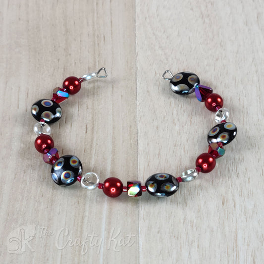 Steel memory wire cuff-style bracelet with red glass pearls, red angle-cut cubes, open silver-plated circles, and silver-dotted black glass coin beads
