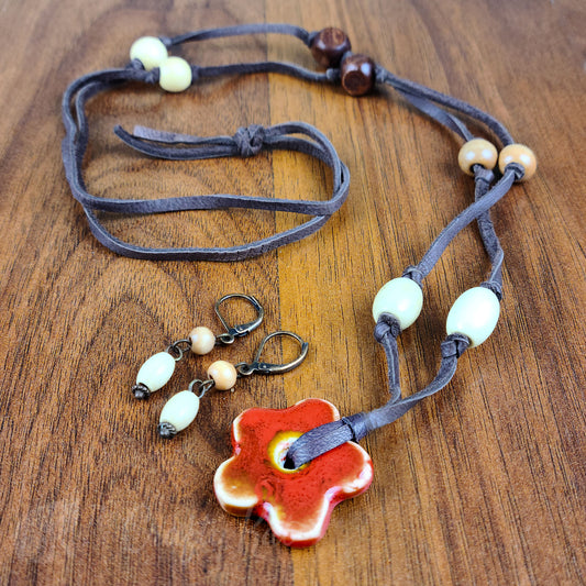 Orange ceramic flower pendant tied on brown suede cord with brown, tan, and cream color wooden beads. Coordinating earrings are cream and tan wooden beads on antique copper fittings.