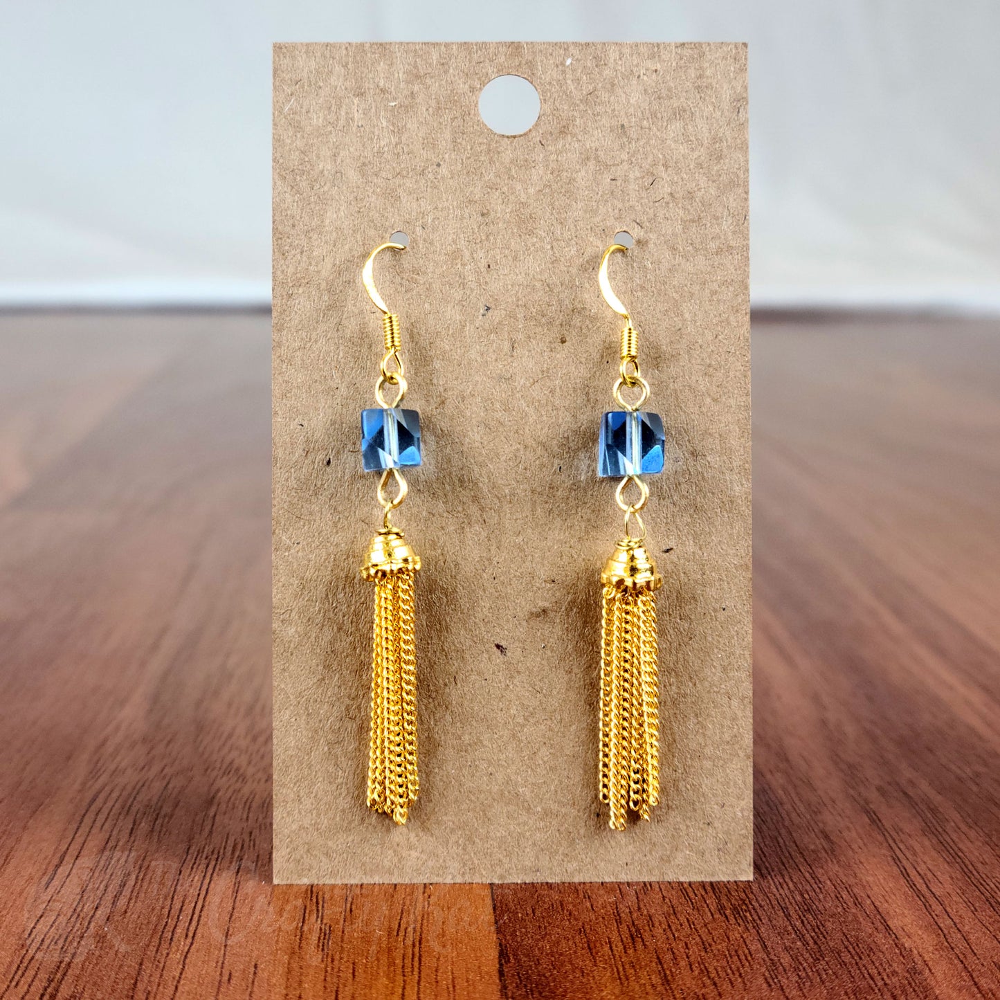 Drop earring featuring an ice blue angle-cut cube crystal bead and gold chain tassle and fittings