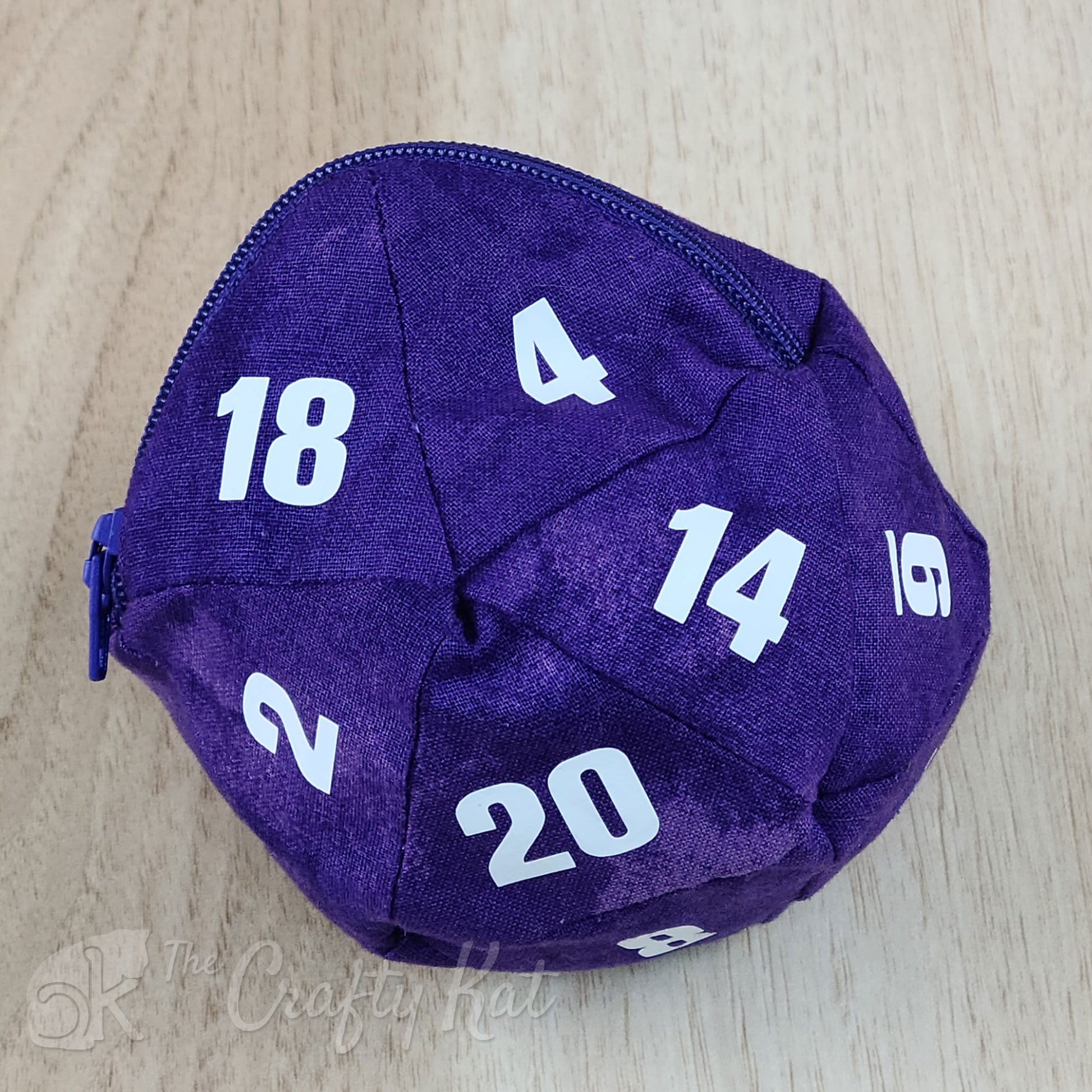 A zippered cotton pouch in the shape of a twenty-sided die, commonly referred to as a d20. The bag shown is purple with white numbers.
