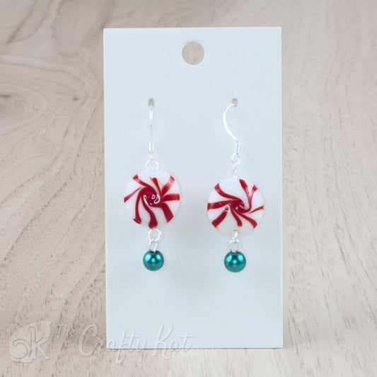 A pair of earrings featuring lampwork glass beads in the shape of classic "starlight" peppermint candies, accented with a dark teal glass pearl on silver base metal.