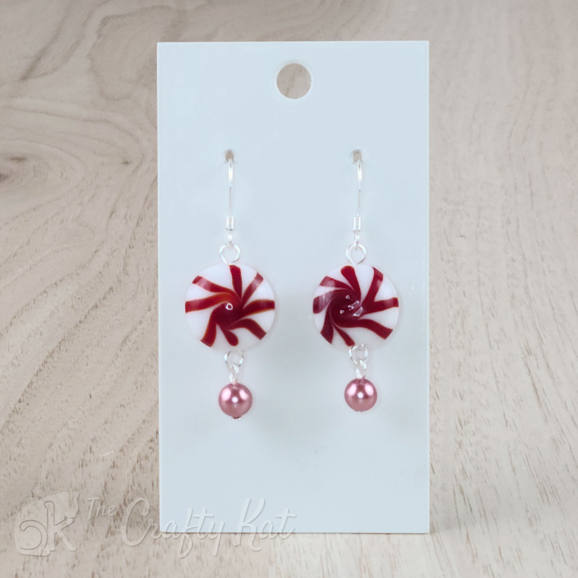 A pair of earrings featuring lampwork glass beads in the shape of classic "starlight" peppermint candies, accented with a pink glass pearl on silver base metal.