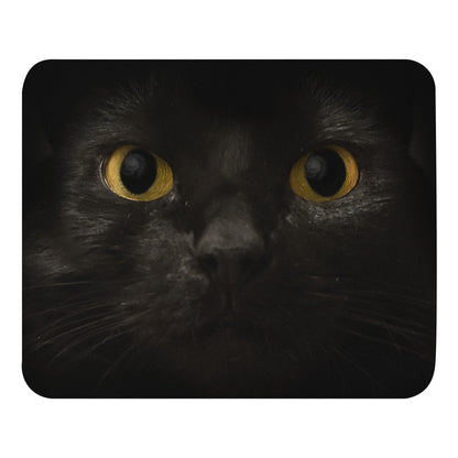 A mouse pad featuring the straight-on face of a black cat with yellow eyes; a galaxy is reflected in her pupils.