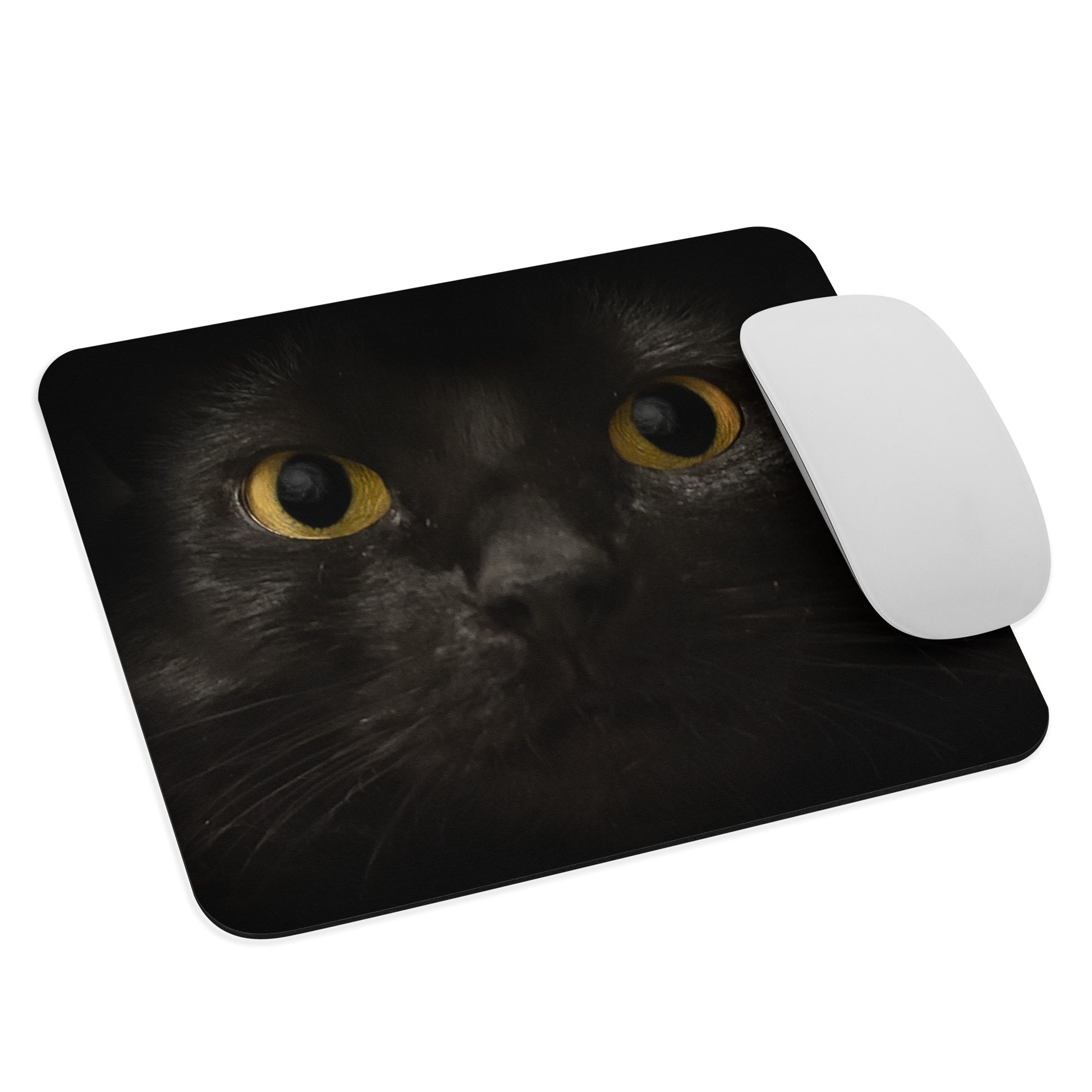 A mouse pad featuring the straight-on face of a black cat with yellow eyes; a galaxy is reflected in her pupils. This mockup includes an Apple mouse for scale.