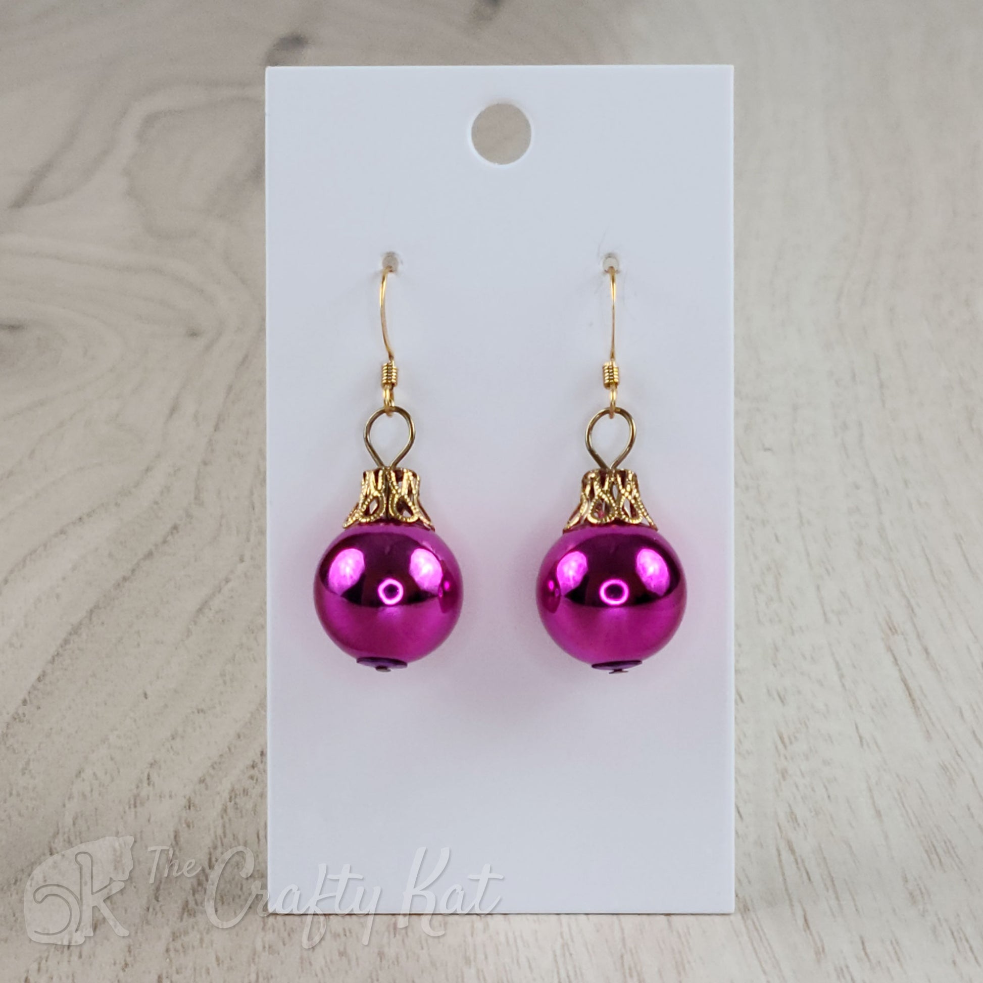 Each earring is a magenta globe with a gold-plated filigree cap, giving each the appearance of a classic holiday tree ornament.
