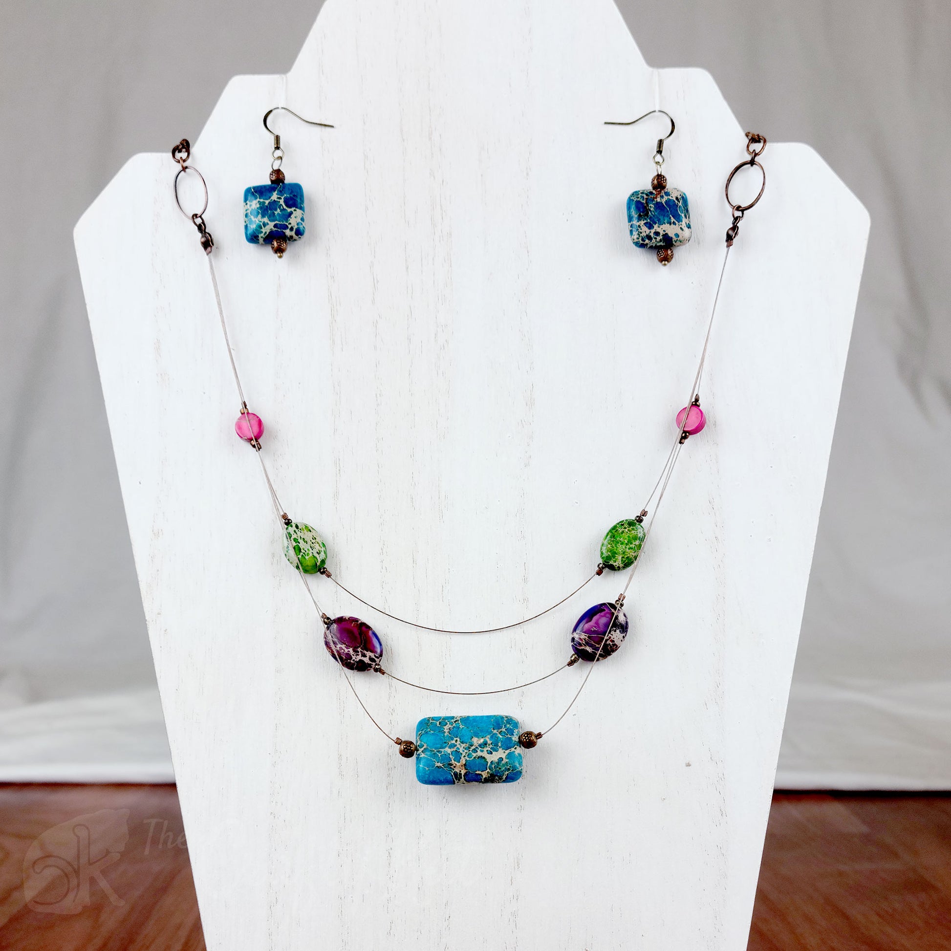 Three-layered tigertail necklace features geometric beads dyed blue, pink, green, and purple; antique copper fittings