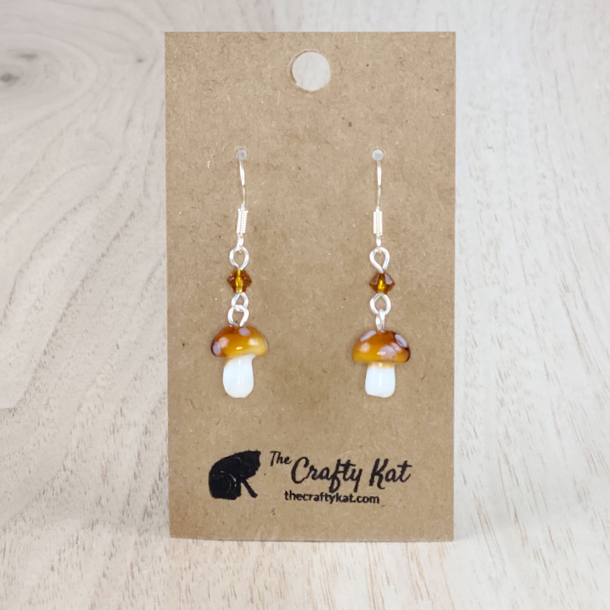 Mushroom-shaped tiered earrings made of lampwork and pressed glass beads with silver-plated base metal fittings. These mushrooms are amber with white spots.