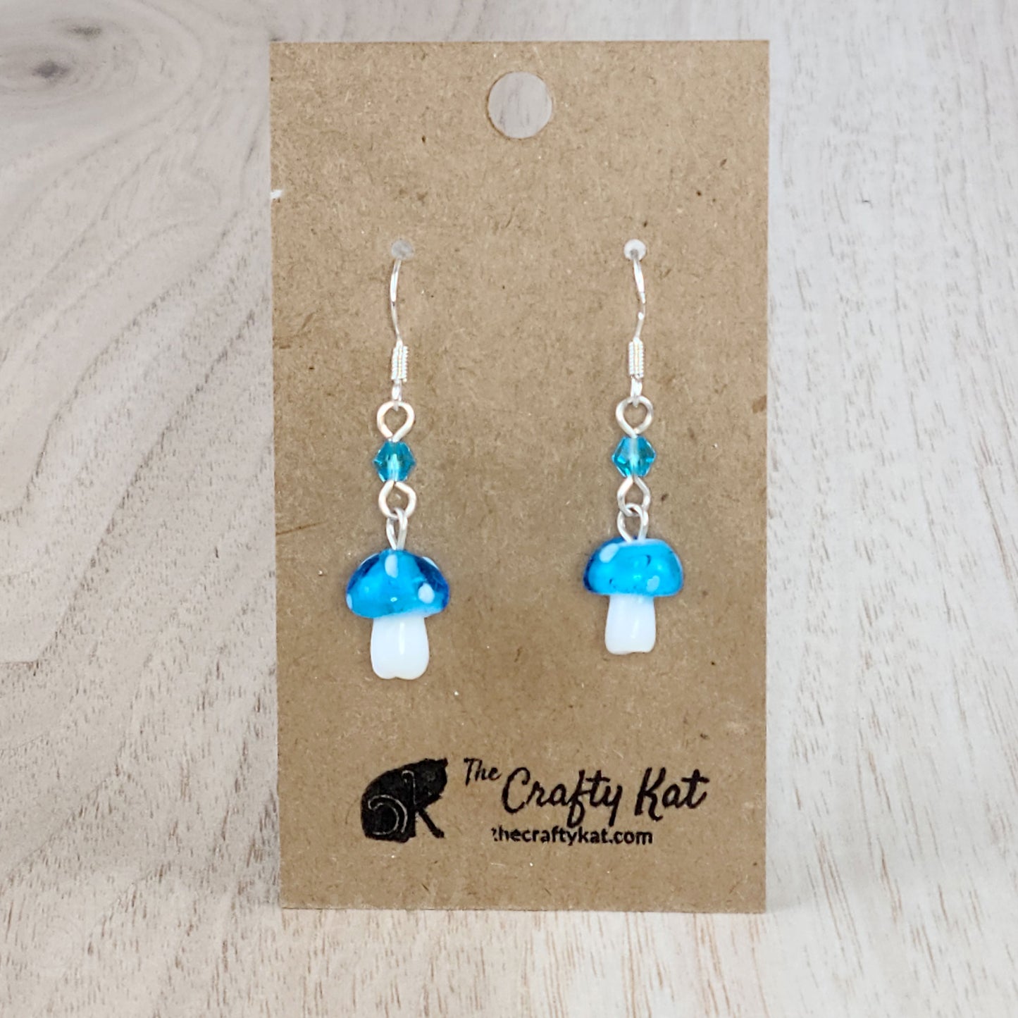 Mushroom-shaped tiered earrings made of lampwork and pressed glass beads with silver-plated base metal fittings. These mushrooms are aqua (sky blue) with white spots.