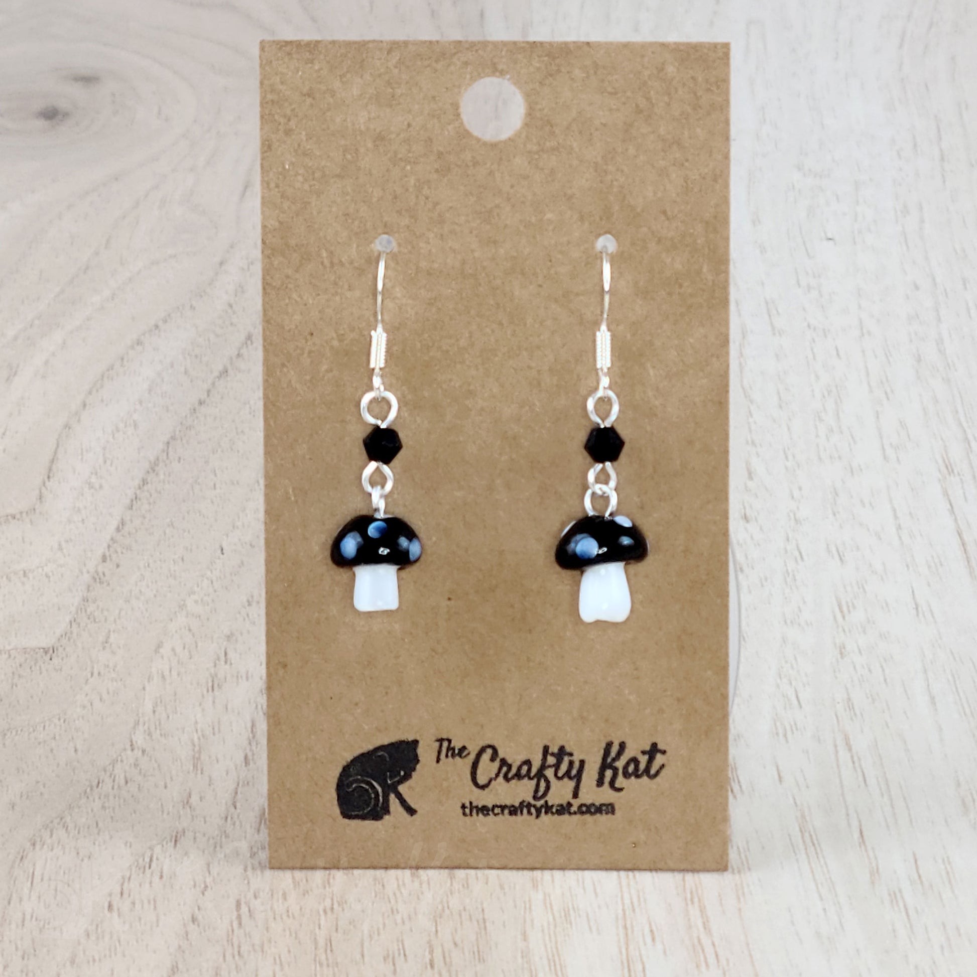 Mushroom-shaped tiered earrings made of lampwork and pressed glass beads with silver-plated base metal fittings. These mushrooms are black with white spots.