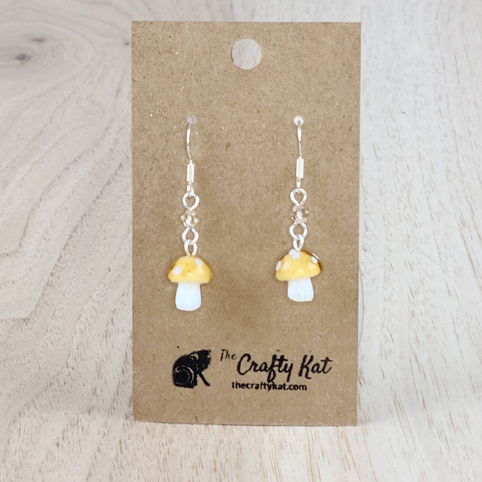 Mushroom-shaped tiered earrings made of lampwork and pressed glass beads with silver-plated base metal fittings. These mushrooms are champagne tan with white spots.
