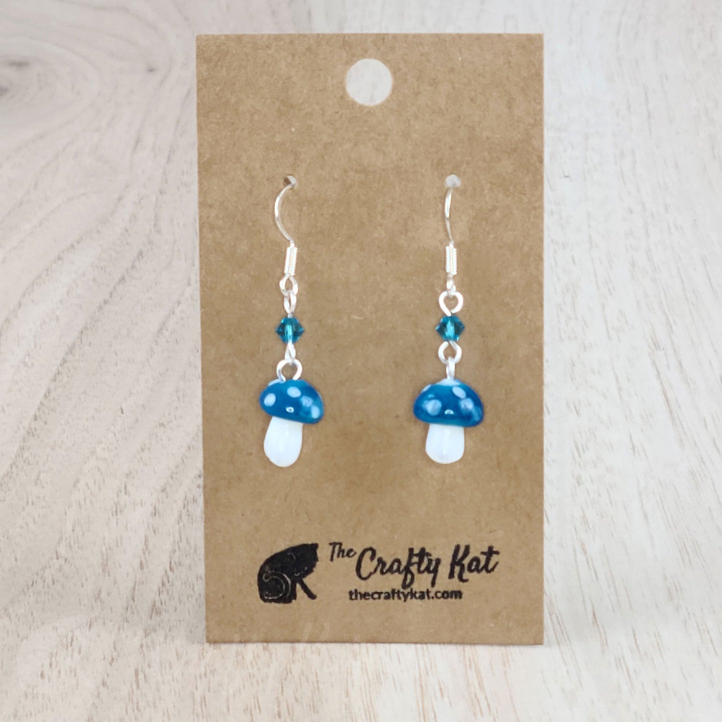Mushroom-shaped tiered earrings made of lampwork and pressed glass beads with silver-plated base metal fittings. These mushrooms are denim blue with white spots.
