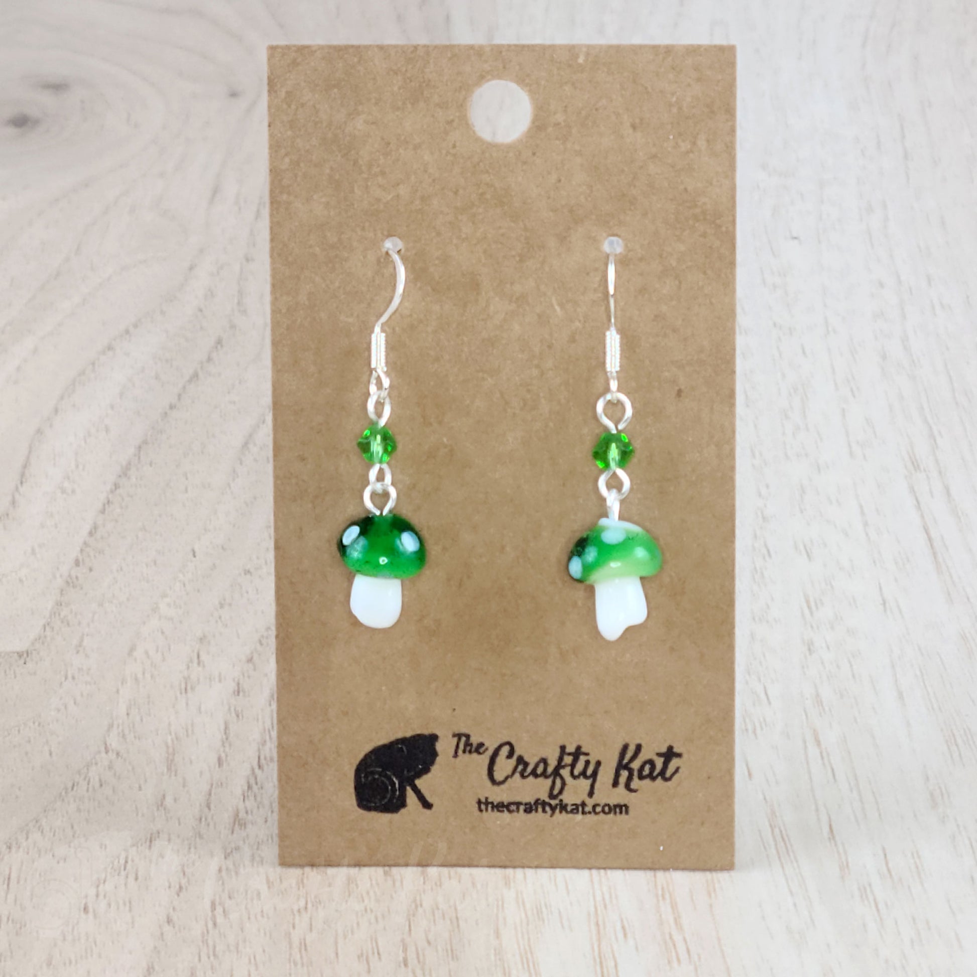 Mushroom-shaped tiered earrings made of lampwork and pressed glass beads with silver-plated base metal fittings. These mushrooms are kelly green with white spots.