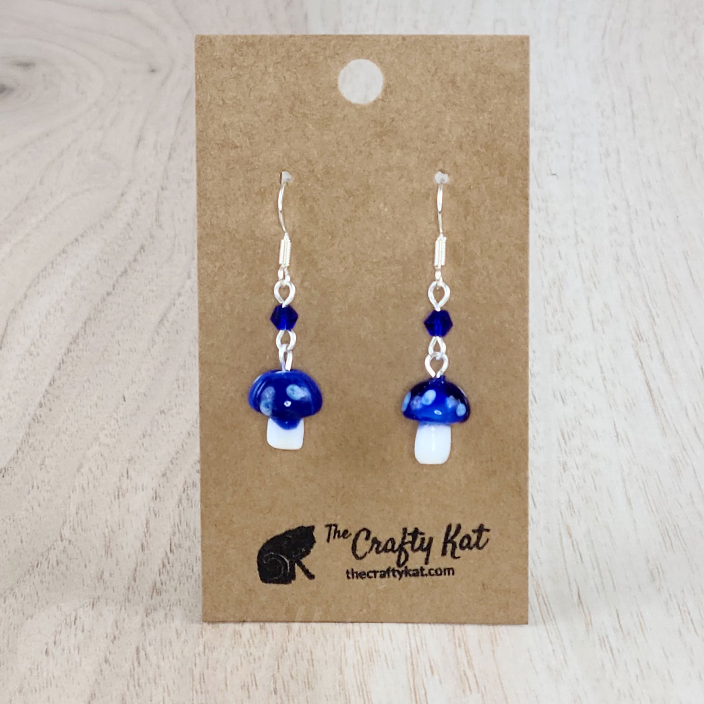 Mushroom-shaped tiered earrings made of lampwork and pressed glass beads with silver-plated base metal fittings. These mushrooms are dark blue with white spots.
