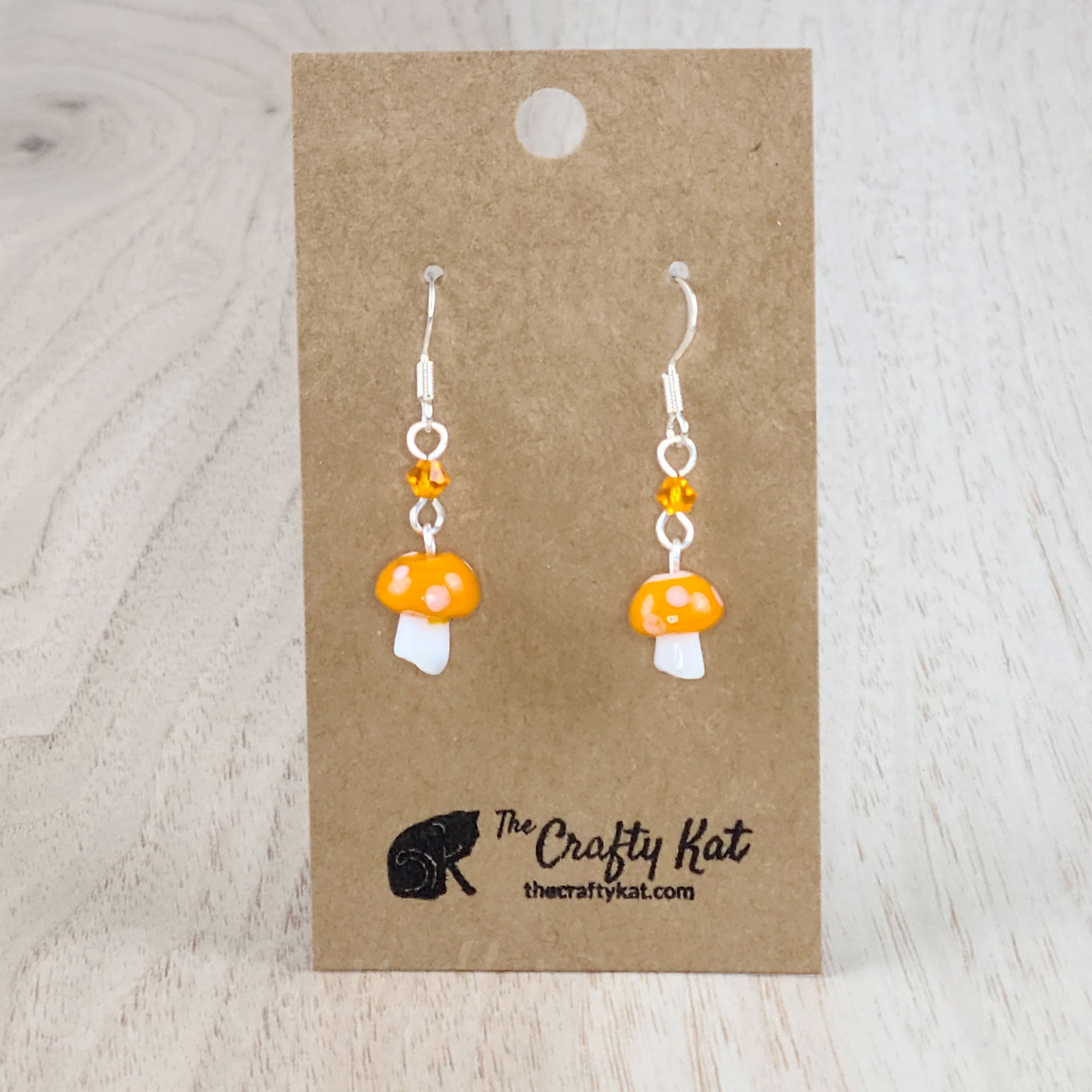 Mushroom-shaped tiered earrings made of lampwork and pressed glass beads with silver-plated base metal fittings. These mushrooms are orange with white spots.