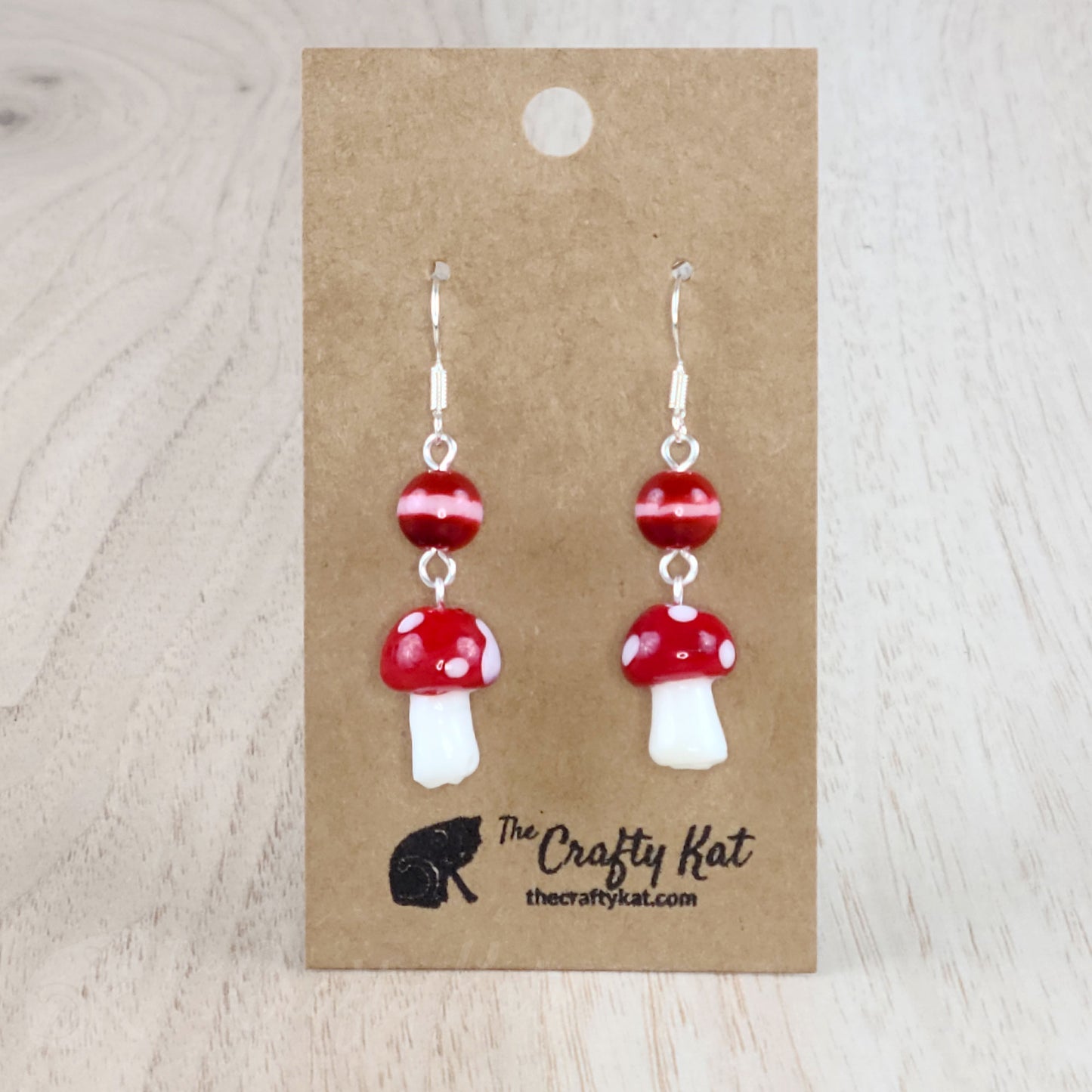 Mushroom-shaped tiered earrings made of lampwork and pressed glass beads with silver-plated base metal fittings. These mushrooms are red with white spots.