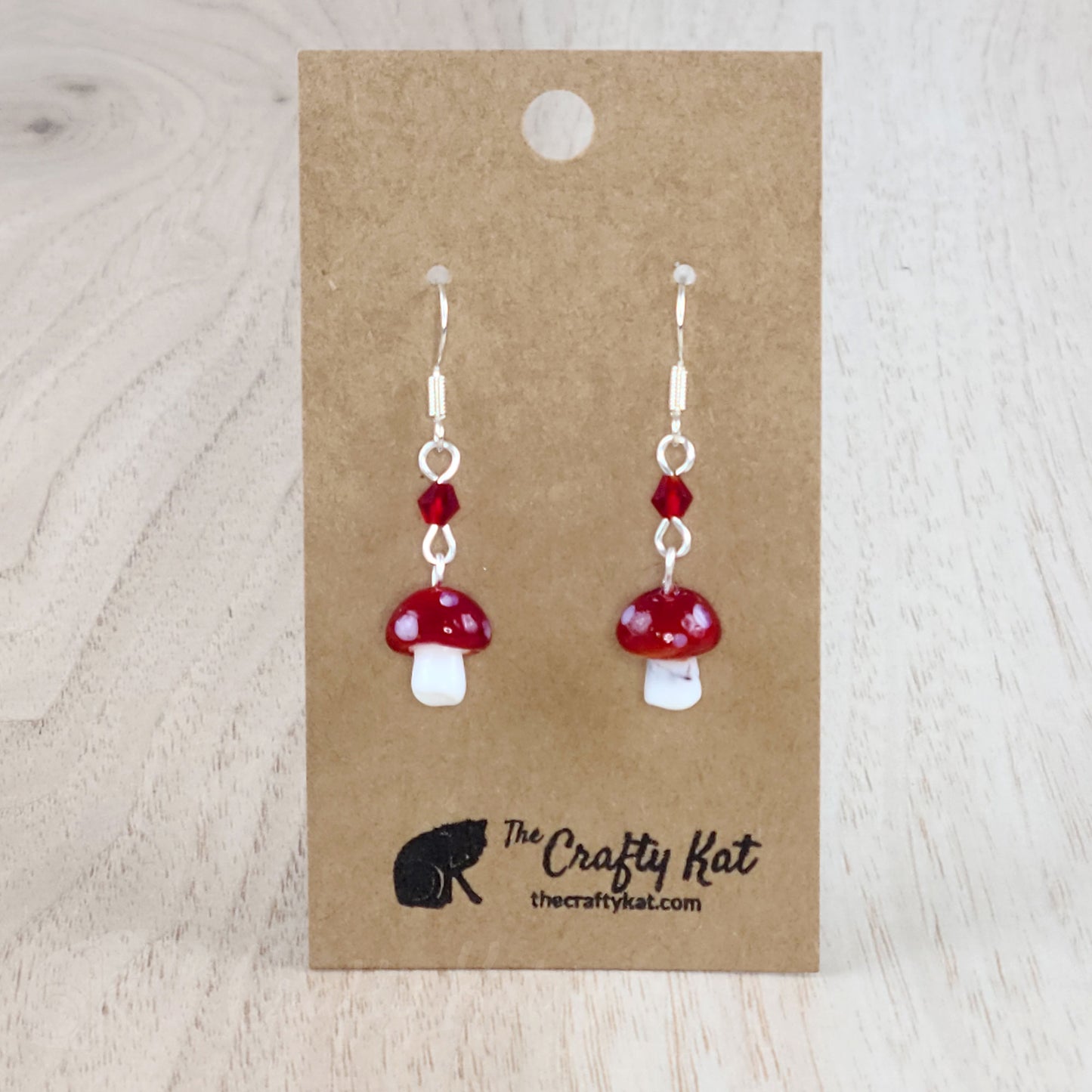 Mushroom-shaped tiered earrings made of lampwork and pressed glass beads with silver-plated base metal fittings. These mushrooms are red with white spots.