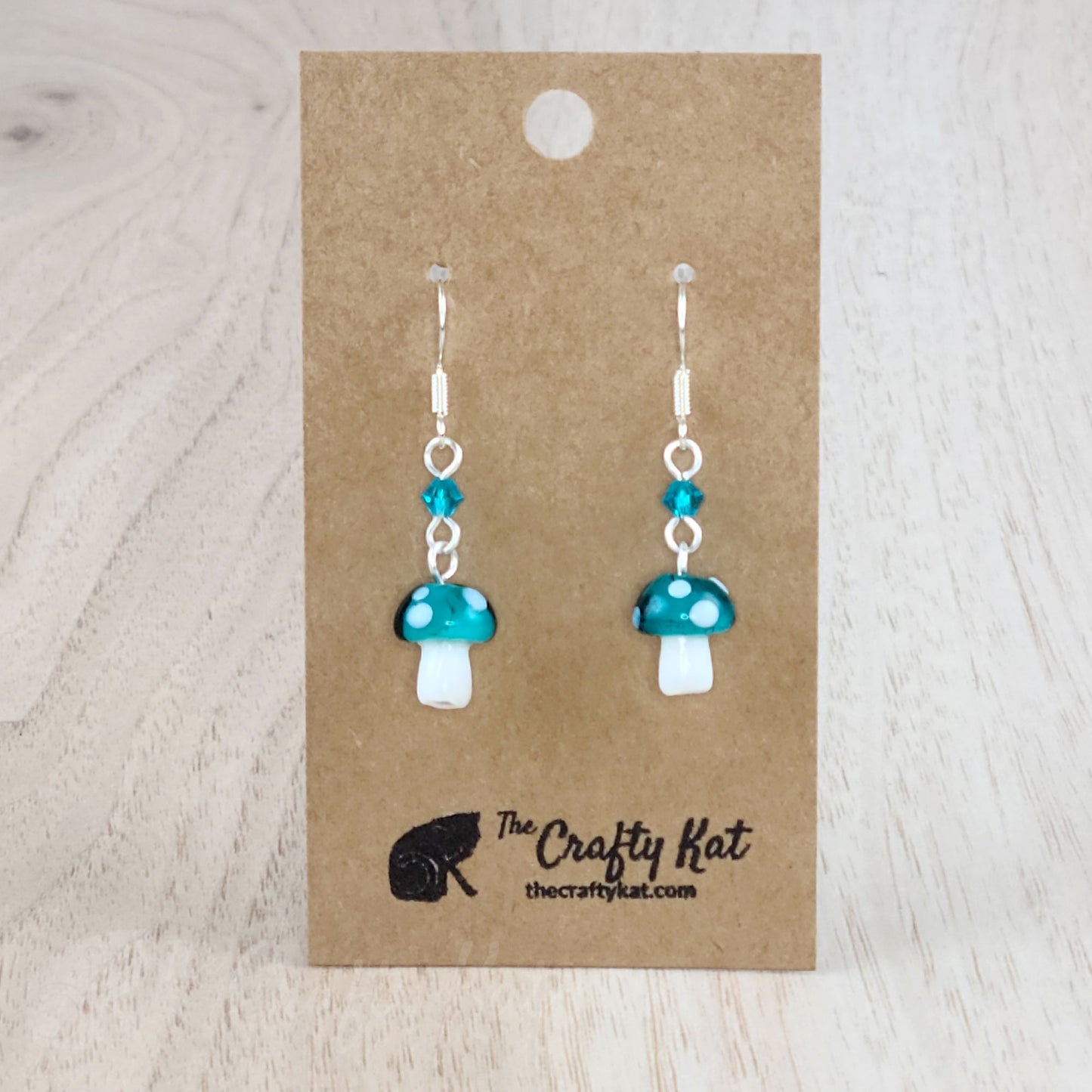 Mushroom-shaped tiered earrings made of lampwork and pressed glass beads with silver-plated base metal fittings. These mushrooms are dark teal with white spots.