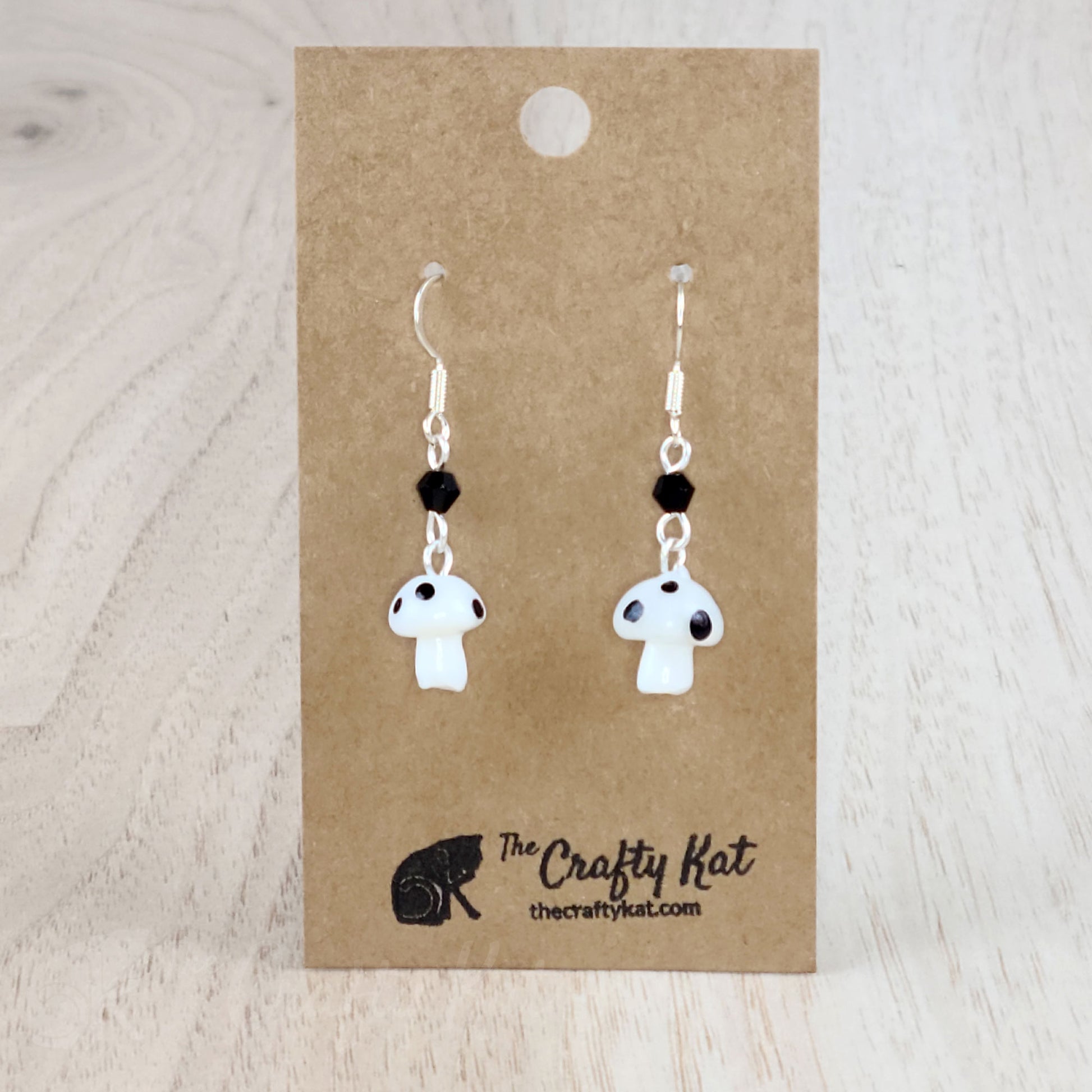 Mushroom-shaped tiered earrings made of lampwork and pressed glass beads with silver-plated base metal fittings. These mushrooms are white with black spots.