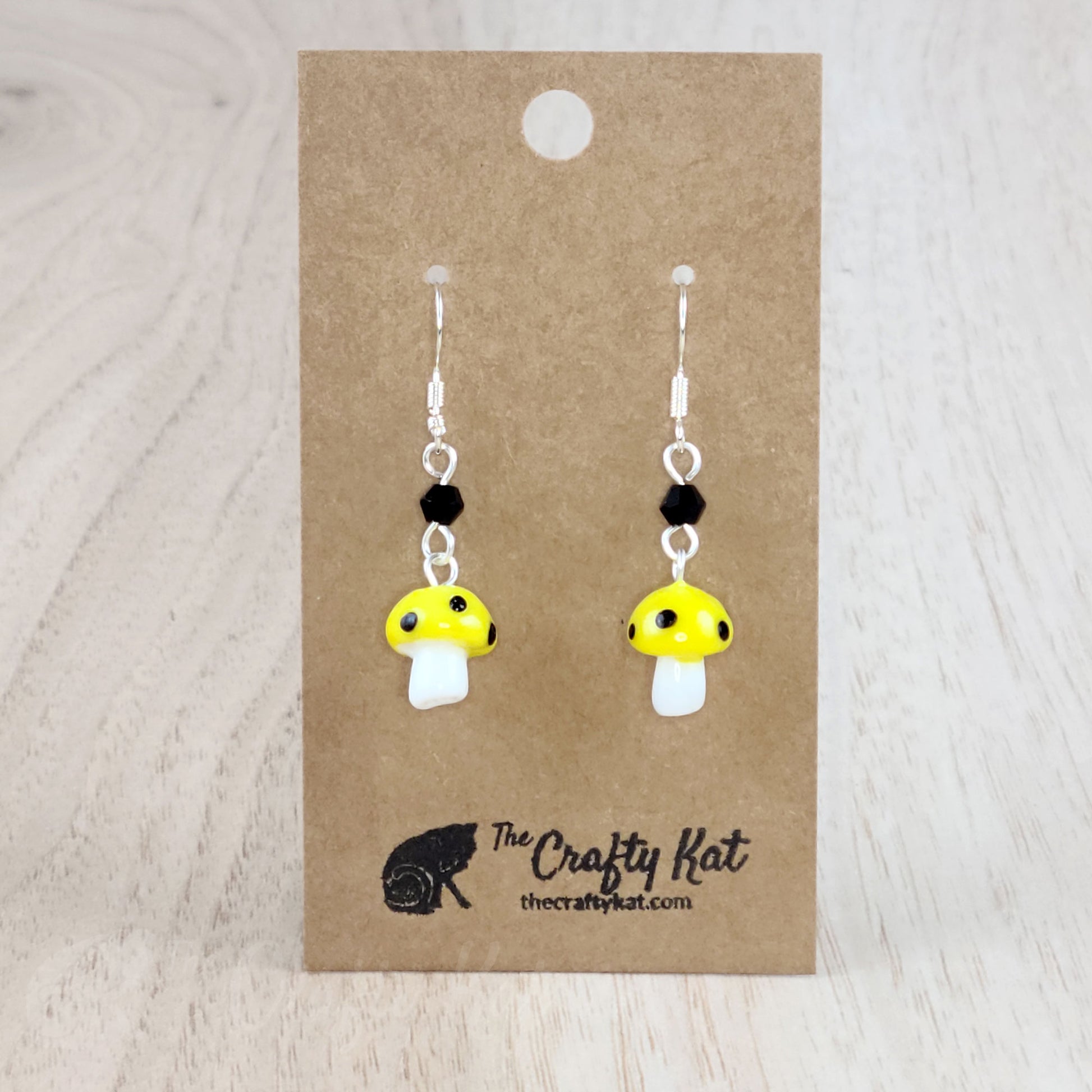 Mushroom-shaped tiered earrings made of lampwork and pressed glass beads with silver-plated base metal fittings. These mushrooms are yellow with black spots.