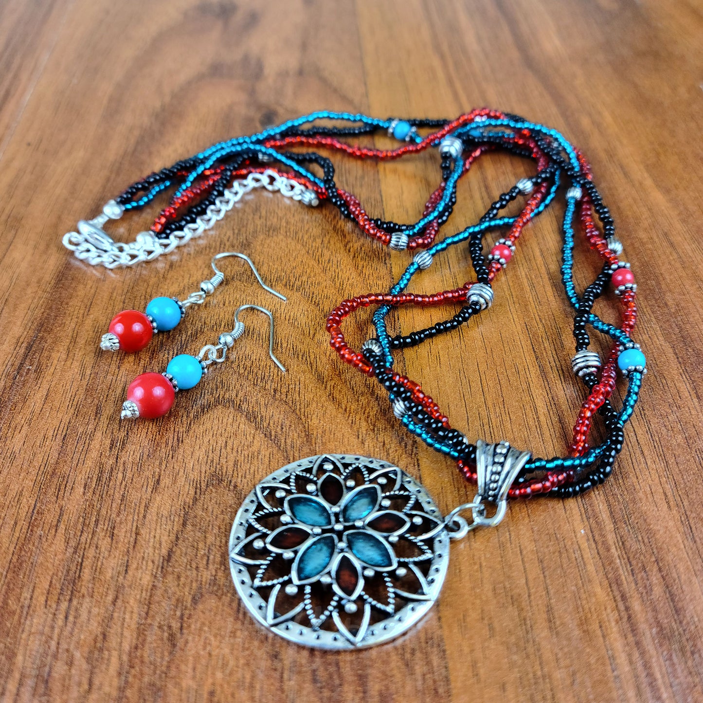 Strands of turquoise, red, and black glass seed beads loosely braided into a strand supporting an antique silver flower pendant filled with turquoise and red enamel; matching turquoise and red resin bead earrings