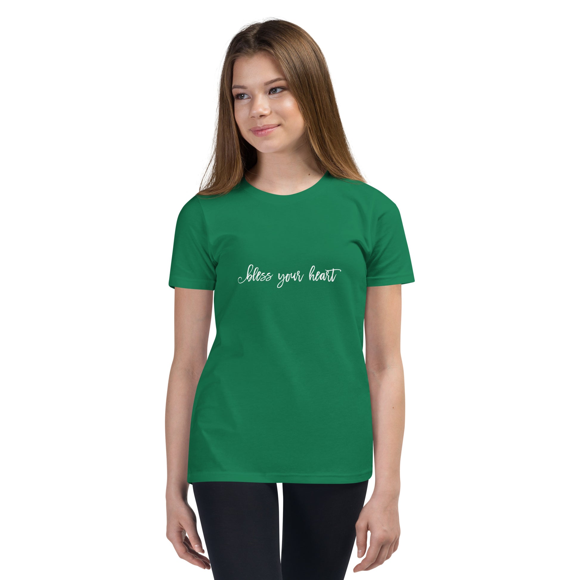 Model wearing Kelly green youth t-shirt with white graphic in an excessively twee font: "bless your heart"