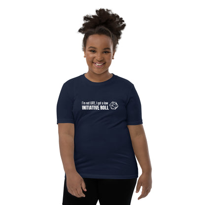 Young female model wearing Navy youth t-shirt with a graphic of a d20 (twenty-sided die) showing a roll of "1" and text: "I'm not LATE, I got a low INITIATIVE ROLL"